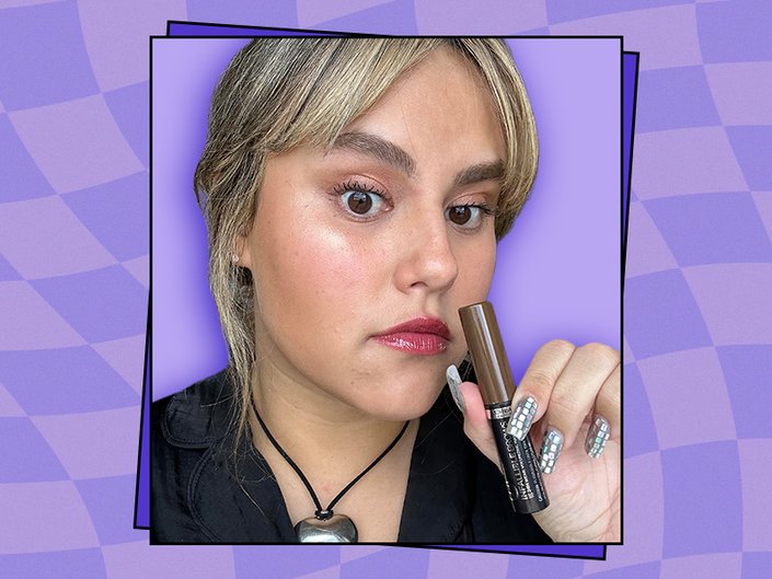 Photo of the editor holding a brow gel on a graphic purple background