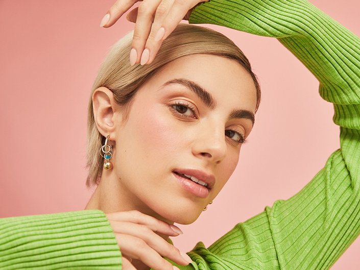 Person with a blonde pixie cut wearing a green sweater and holding their hands around their face