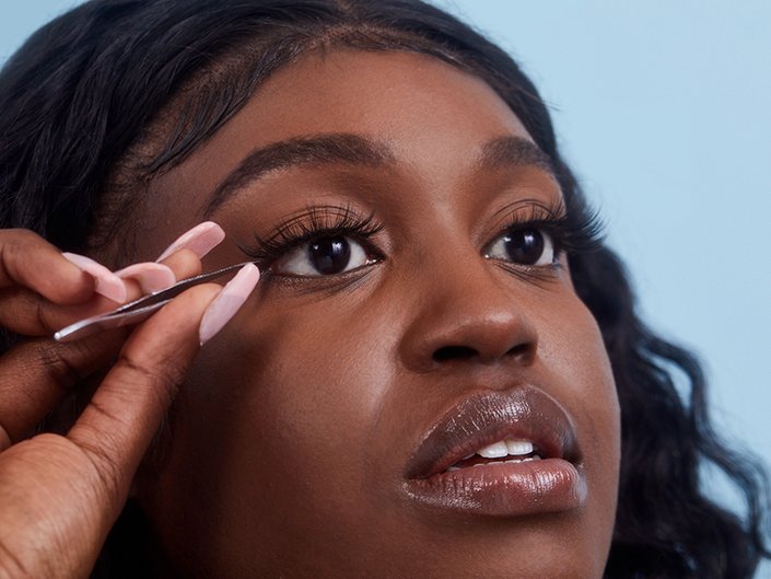 person holding false eyelash strip to eyelashes with tweezers
