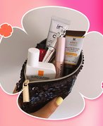 Photo of a person with yellow painted nails holding an unzipped black sequin makeup bag filled with various beauty products, collaged on a pink tie-dye background