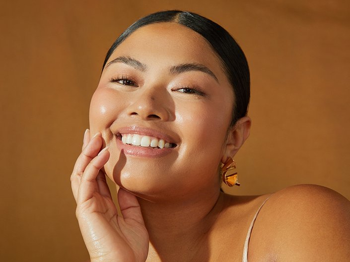 Close-up picture of a model smiling at the camera with their hand on their chin