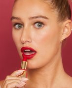 Person wearing red lipstick and holding the lipstick up to their lips with their mouth open