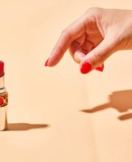 A hand with red nail polish reaching for red YSL Beauté Rouge Volupté Shine Lipstick Balm