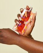 Picture of someone holding a bottle of perfume and rubbing their wrists together to apply
