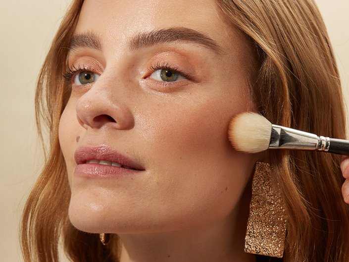 Person applying bronzer to their cheekbones